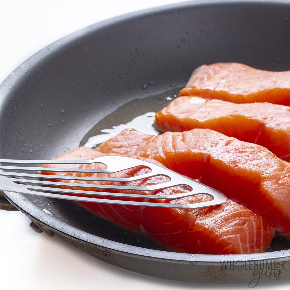 Frying salmon with fish spatula holding fillet down.